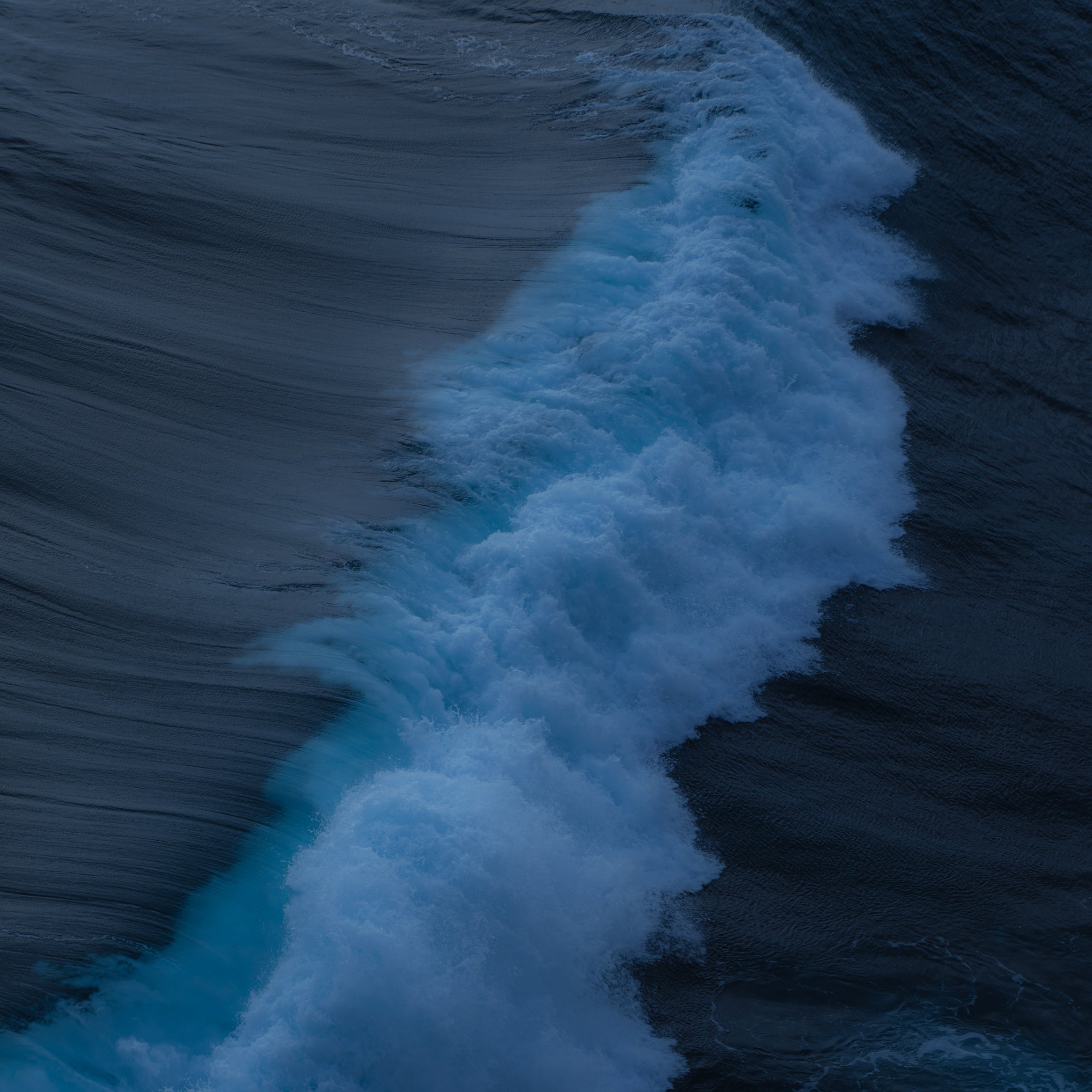 Close-up of a wave crashing on a rocky shore with dark blue water.